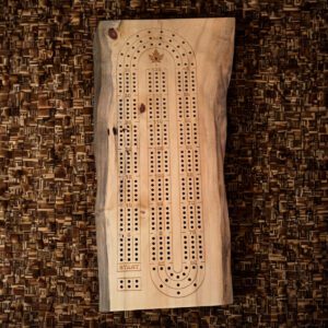 Live edge wooden cribbage board carved from Manitoba maple, showing natural grain, knots, and a smooth playing surface on a rustic table.