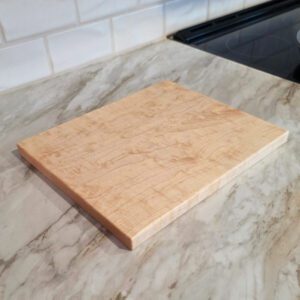 Maple cutting board standing upright on a kitchen counter with white tile backsplash