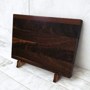 Handcrafted black walnut cutting board displayed upright, showcasing natural grain variation